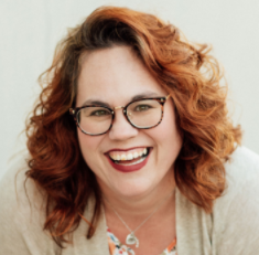 Woman with brown wavy hair and glasses smiling